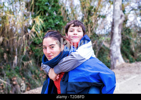 oung boy piggyback on his sister looking at camera and smiling in nature Stock Photo