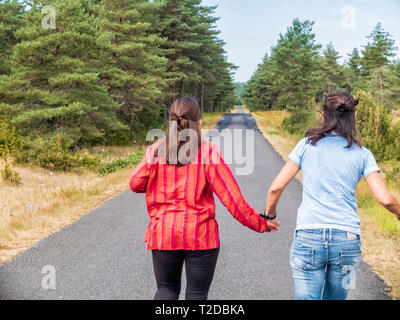 Back view of two friends running side by side on road holding hands Stock Photo