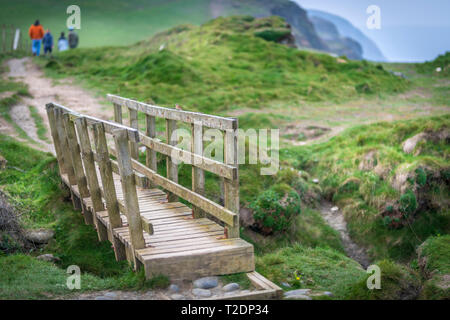 Walkers use a small wooden bridge to cross over uneven terrain on the popular South West Coast Path near Abbotsham in North Devon. Stock Photo