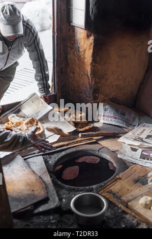 Locals queue in the cold, early morning light for freshly cooked bread from the tan door oven. Leh, Ladakh, India. Stock Photo