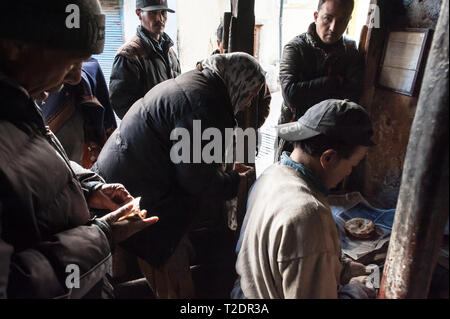 Locals queue in the cold, early morning light for freshly cooked bread from the tan door oven. Leh, Ladakh, India. Stock Photo