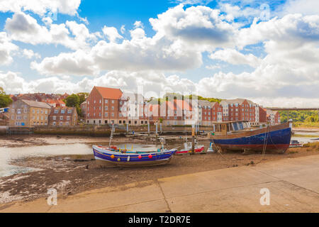 Fishing boats moored up on the dry banks of Whitby harbour with back drop of houses across the harbour Stock Photo