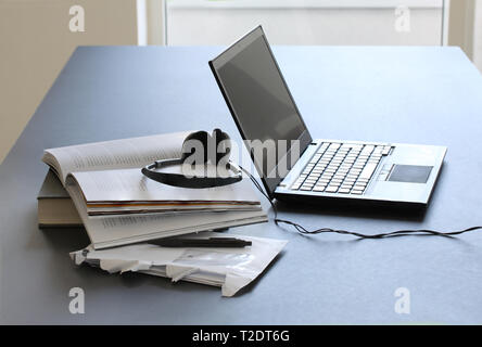 Laptop computer on working table with books, papers, pencil and headphones Stock Photo