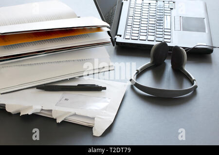 Laptop computer on working table with books, papers, pencil and headphones Stock Photo
