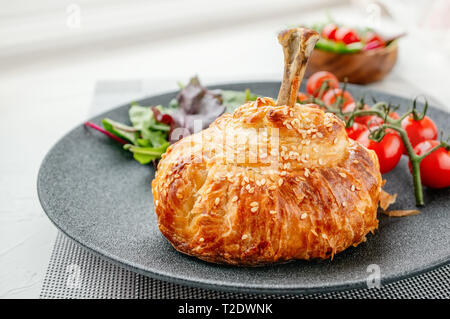 Chicken drumstick in dough baked in the oven with potatoes, tomatoes, onions and spices with a side dish of tomatoes and green salad. Stock Photo