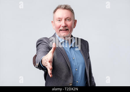 Handsome european senior man in suit and blue shirt saying hello, shaking hand. Welcome home sign Stock Photo