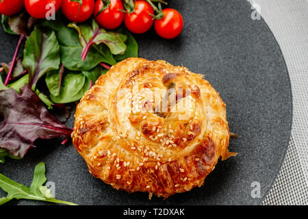 Chicken drumstick in dough baked in the oven with potatoes, tomatoes, onions and spices with a side dish of tomatoes and green salad. Stock Photo