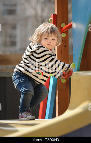cute little blond toddler girl climbing and sliding down the children's slide at playground Stock Photo