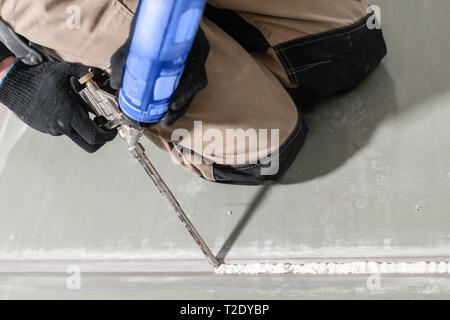 Worker is using a polyurethane foam for gluing drywall at ninety degrees. Hand holding polyurethane expanding foam glue gun applicator. Stock Photo
