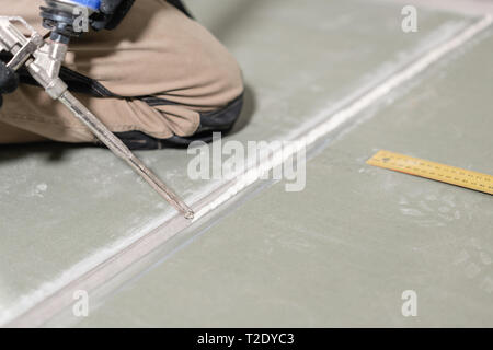Worker is using a polyurethane foam for gluing drywall at ninety degrees. Hand holding polyurethane expanding foam glue gun applicator. Stock Photo