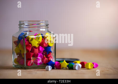 Multicolor paper star in square glass bottle on wooden table with morning sunlight. Stock Photo