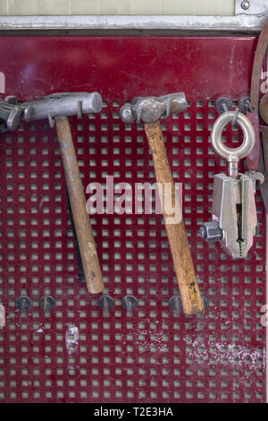 Vertical view of two old hammers with a brown wooden handle and a clamp hanging on the wall in a workshop for carpentry work on a red background Stock Photo