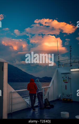 Two lovers with the back to the camera looking amazed at a cloud formation while on deck on the ferry with Samothrace Island in the background Stock Photo