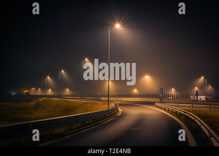 Highway exit during a foggy night with street lights and signs on the asphalt Stock Photo
