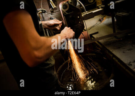 Male sharpening knife on linisher machine in workshop Stock Photo