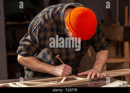 experienced carpenter in work clothes and small buiness owner measures a wooden board with a marks with pencil the necessary points for slices Stock Photo