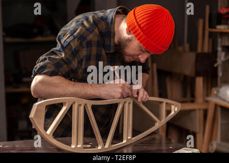 experienced carpenter in work clothes and small buiness owner measures a wooden board with a marks with pencil the necessary points for slices Stock Photo