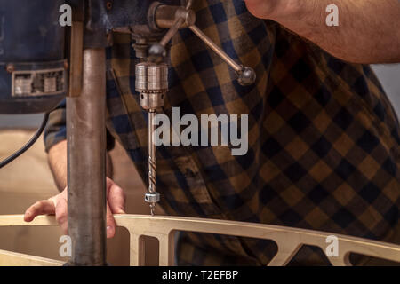 Close up of experienced carpenter in work clothes and small buiness owner  is carving a wooden board on an  modern  hand drill in a light workshop sid Stock Photo