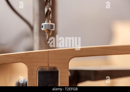 Close up of a man with work clothes and a carpenter's hat is carving a wooden board on an  large drilling machine in a light workshop Stock Photo