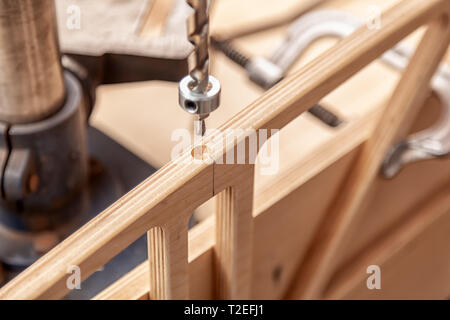 Close up of a man with work clothes and a carpenter's hat is carving a wooden board on an  large drilling machine in a light workshop Stock Photo