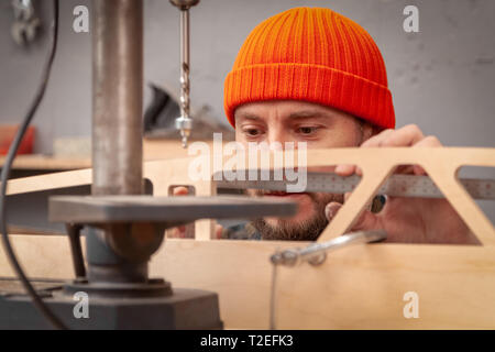 Profesional drilling wood on vertical drill machine. Close up of a metal drill making holes in the wood. Stock Photo