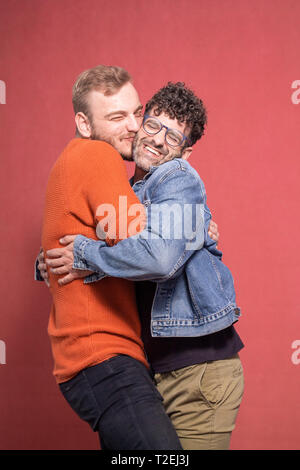 two men, cutest cuddling gay couple ever. shot in studio (pink background), smiling and happy together. cuteness overload. Stock Photo