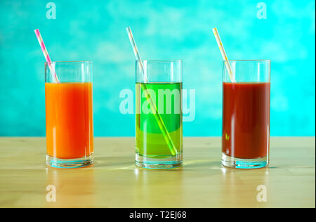 Fresh orange, apple and tomato juices in glasses with paper straws in bright table setting. Stock Photo