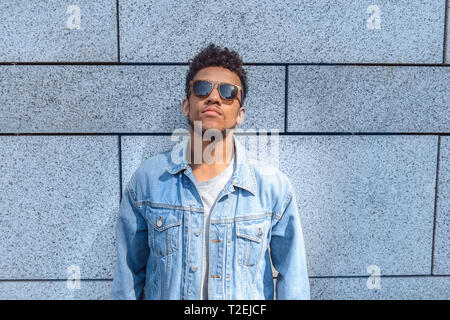 Young mulatto man wearing sunglasses standing isolated on concrete wall leaning back looking up relaxed Stock Photo