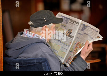 Profile of senior man in casual dress reading the racing pages of a daily Red Top newspaper Stock Photo