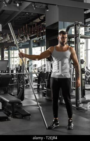 Bearded man bodybuilder exercising at gym holding bar looking aside pensive full body shot Stock Photo