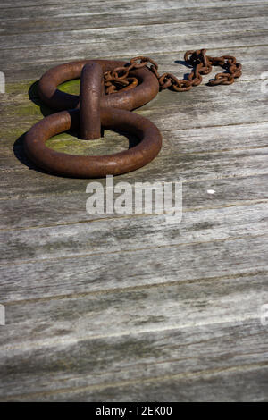 Low angle portrait view of two rusty weathered mooring rings with smaller chain on timber board decking