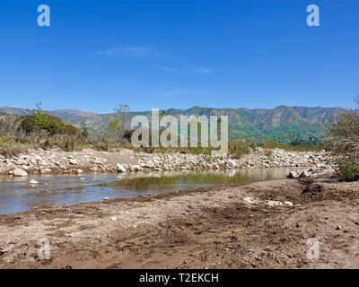 Large rocks, stones, line the edges of the Ventura River with Topatopa Mountains in the background, Ojai, California, USA Stock Photo