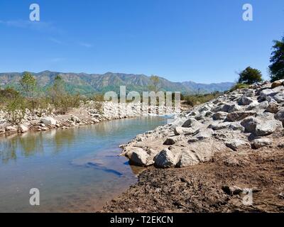 Large rocks, stones, line the edges of the Ventura River with Topatopa Mountains in the background, Ojai, California, USA Stock Photo