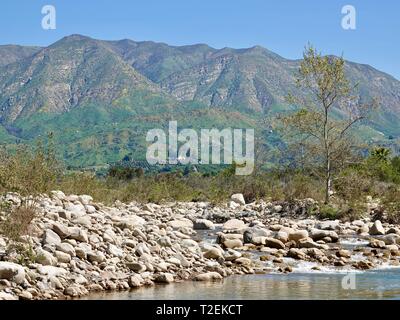 Large rocks, stones, line the edges of the Ventura River with Topatopa Mountains in the background, Ojai, California, USA Stock Photo