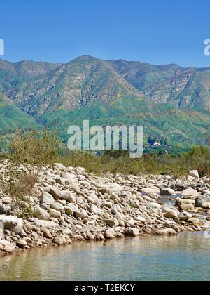 Large rocks, stones, line the edges of the Ventura River with Topatopa Mountains in the background, Ojai, California, USA Stock Photo