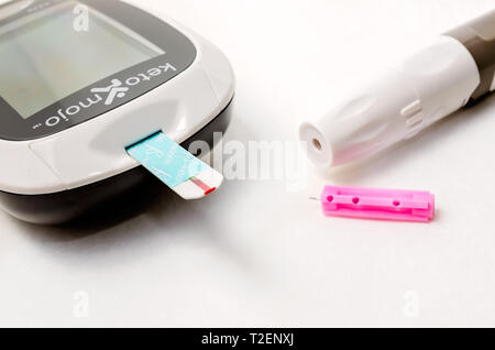 A Keto-Mojo ketone and blood glucose meter is pictured on white, along with a ketone test strip, lancet device and disposable lancet, March 30, 2019,  Stock Photo
