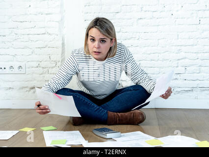 Portrait of worried young woman feeling stressed and desperate on the ground with calculator accounting expenses not able to pay mortgage. In paying d Stock Photo