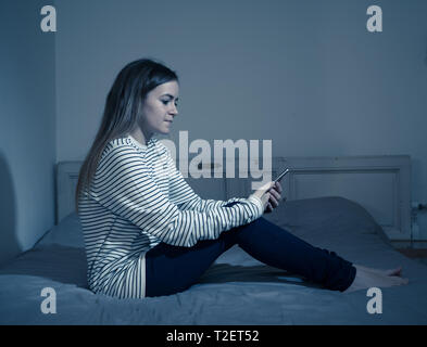 Young teenager girl suffering mobile cell phone addiction feeling lonely and depressed having insomnia needing to be connected sitting on bed late at  Stock Photo