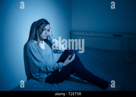 Young teenager girl suffering mobile cell phone addiction feeling lonely and depressed having insomnia needing to be connected sitting on bed late at  Stock Photo