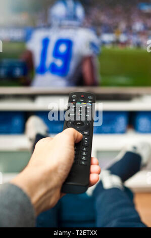man hand holding a remote control pointed to a television screen Stock Photo