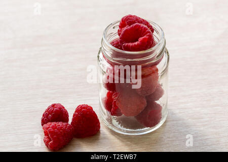 Glass jar with raspberry and three berries on the wooden table. Summer ripe juicy raspberries. Stock Photo