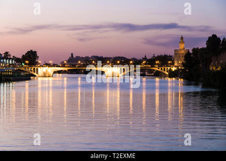 Sevilla, Spain. Views of the Guadalquivir river, with the Torre del Oro (Tower of Gold) and the Puente de San Telmo bridge at sunset Stock Photo