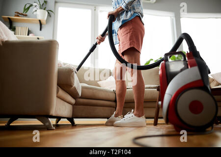 Unrecognizable woman in shorts cleaning sofa with vacuum cleaner while removing dust and fur in living room Stock Photo