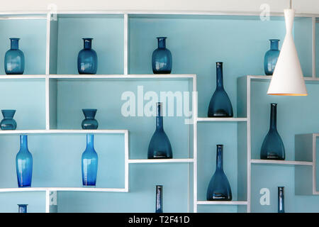 Retro style blue glass bottles in a beautiful arrangement on shelves attached to a light blue wall. Stock Photo