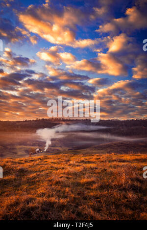 Gorgeous rural scene with a small house in a valley surrounded by fog and smoke from a fire in the morning and an incredible sky with blue sky and dra Stock Photo