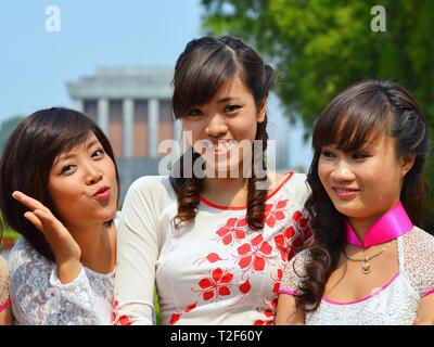 Three dressed-up Vietnamese girls wear traditional Vietnamese silk dresses (áo dài) and pose for the camera in front of the Ho Chi Minh Mausoleum. Stock Photo