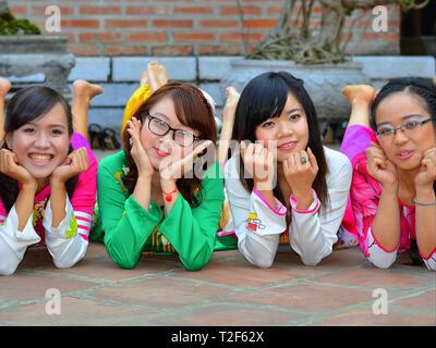 Four dressed-up Vietnamese girls in a prone position rest their heads on their hands and look at the camera. Stock Photo