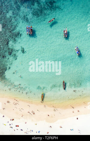View from above, aerial view of a beautiful tropical beach with white sand and turquoise clear water, long tail boats and people sunbathing. Stock Photo