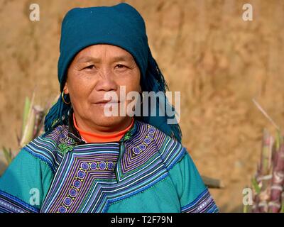 Elderly Vietnamese Flower H’mong hill-tribe market woman wears embroidered, colourful Flower H’mong traditional attire and poses for the camera. Stock Photo
