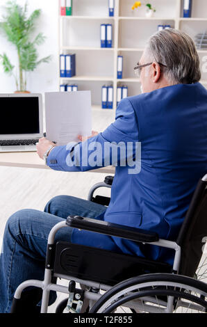 Aged employee in wheelchair working in the office Stock Photo